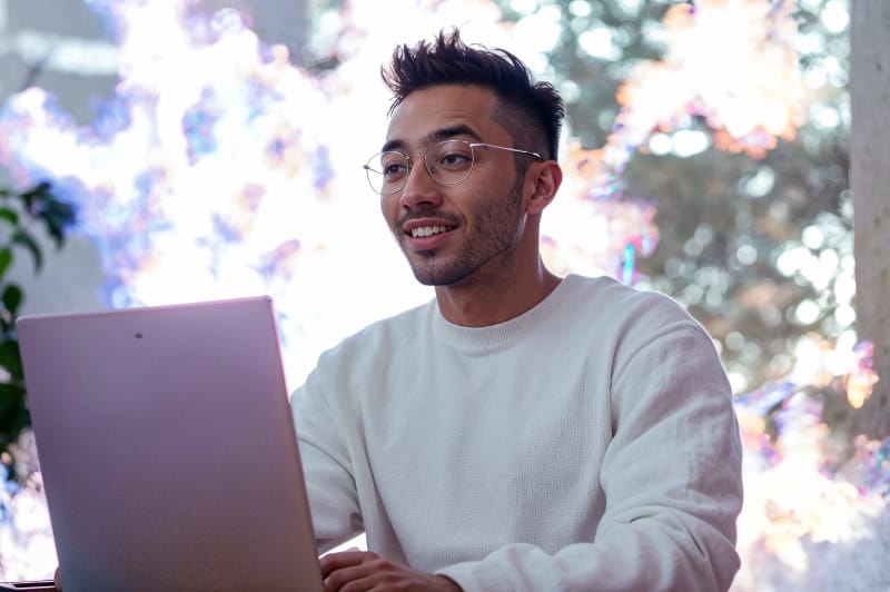 Hombre con sudadera blanca y gafas escribiendo en un ordenador portátil