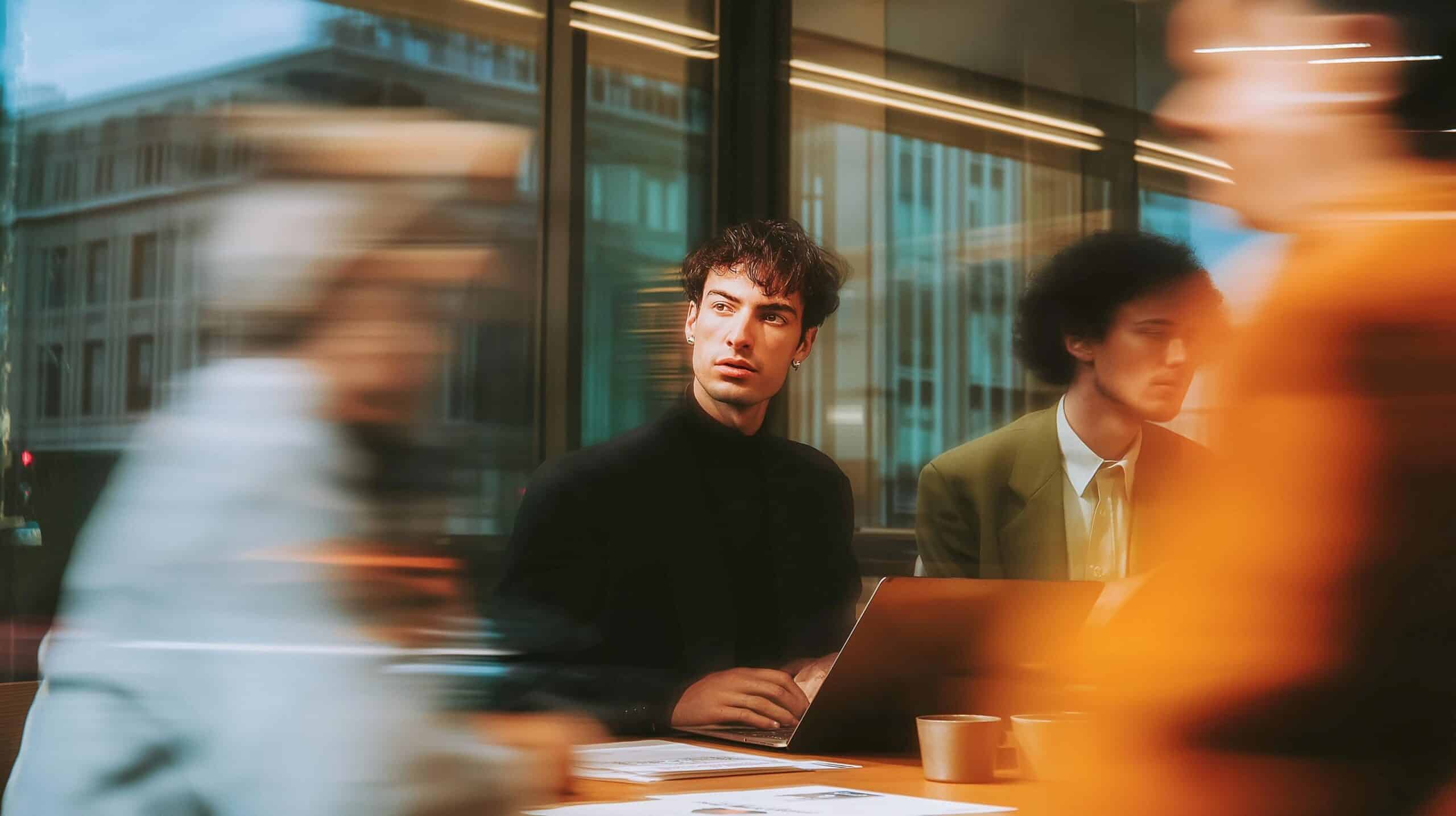 Dos profesionales conversando en una oficina moderna, con movimiento de personas en primer plano, representando la adaptación empresarial a la Ley de IA de la Unión Europea.